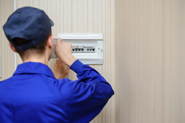 Wall Mural - back view of a young eletrician in blue overall disassembling a electrical panel with fuses in a house.