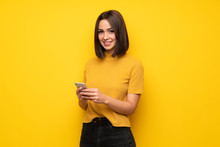 Young Woman Over Yellow Wall Sending A Message With The Mobile