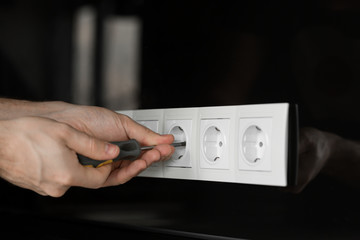 Close-up of an electrician's hand with a screwdriver disassembling a white electrical outlet on a black glass wall