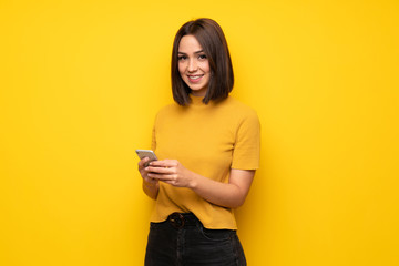 young woman over yellow wall sending a message with the mobile
