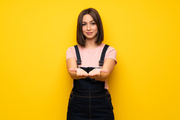 Young woman over yellow wall holding copyspace imaginary on the palm to insert an ad