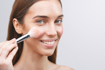 Young girl applies powder on the face using makeup brush