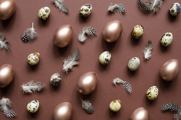 Wall Mural - Easter holiday background. Easter egg composition of painted eggs, quail eggs and feathers on brown background.