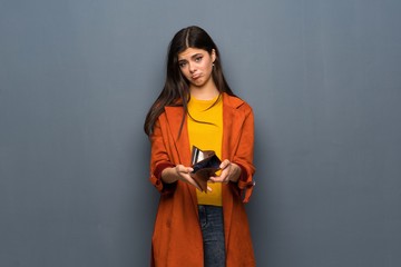 Wall Mural - Teenager girl with coat over grey wall holding a wallet