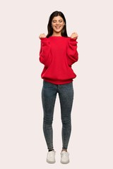 A full-length shot of a Teenager girl with red sweater celebrating a victory in winner position over isolated background