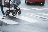 Fototapeta Sawanna - women with a stroller or buggy is crossing a wet street on a pedestrian crossing