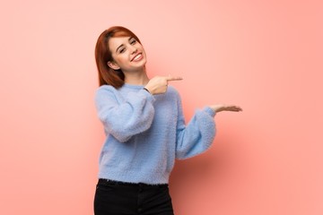 Wall Mural - Young redhead woman over pink background holding copyspace imaginary on the palm to insert an ad