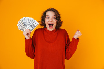 Wall Mural - Excited happy young pretty woman posing isolated over yellow wall background holding money.