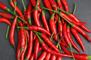 A lot of sharp hot spice red chilli cayenne pepper with wet drops of freshness water dew on a black graphite slate stone surface. Natural vegeterian diet organic vegetable. Dark food foto