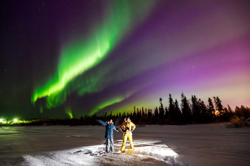two young men are posing against shining northern lights sky
