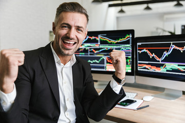 Fototapete - Photo of happy businessman rejoicing while working in office with digital graphics and charts