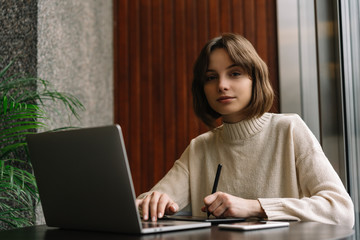 Graphic designer freelancer working project, using laptop computer and digital drawing tablet, develop design for web. Portrait of successful photographer retouching image at workplace. Remote work 