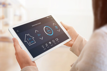 Poster - Modern home control app with flat interface on tablet display. Woman holding tablet. Sun light in background. Close-up.
