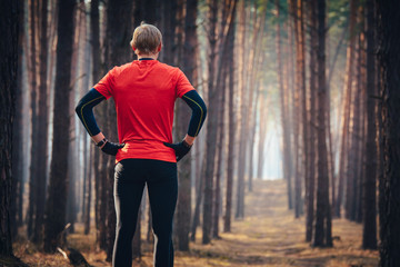 Wall Mural - Athlete focusing on training, standing in red shirt in morning pine forest before trail training run