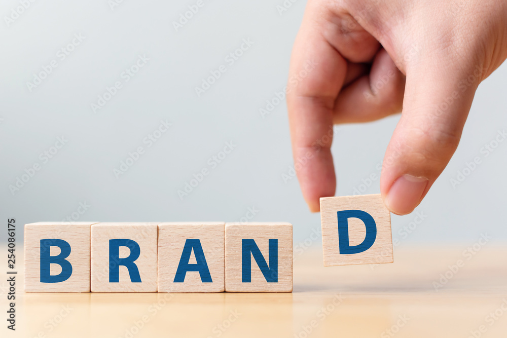 Hand of male putting wood cube block with word “BRAND” on wooden table. Brand building for success concept - obrazy, fototapety, plakaty 