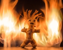 A Needle Punched Voodoo Doll Stands In Front Of A Bright Fire