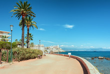 The Pedestrian Promenade Along The Coast Of The French Town Of Antibes With The Old City Wall And Center In The Distance