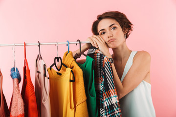 Wall Mural - Woman stylist posing isolated over pink wall background near a lot of clothes.