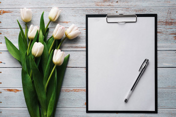 Wall Mural - White bouquet of tulips on wooden blue background with blank paper tablet
