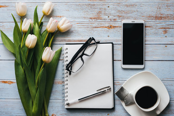Wall Mural - White bouquet of tulips on wooden background with coffee Cup, a smartphone and an empty notebook