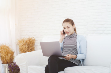 Beautiful Asian woman is smiling.Asian women work with gray laptops on the sofa in the room in the morning.Orange shopping bag in his hand.Girl in white shirt.