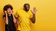 © wayhome.studio  - Optimistic black female and male enjoys favourite moment in song, smile from joy and pleasure, dance while listen music in headphones, sing aloud, isolated over yellow wall with free space right