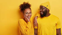 Happy Afro American Couple In Fashionable Neat Clothes, Express Joy, Have Pleasant Friendly Talk, Cheerful Expressions, Enjoy Togetherness, Isolated Over Yellow Background. Friendship And Partnership