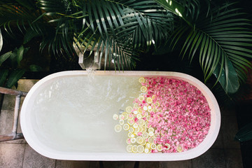 Bath tub filling with water with flowers and lemon slices