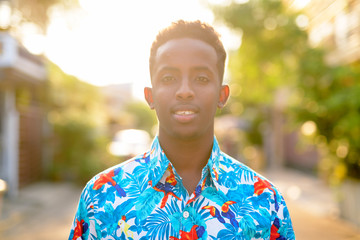 Face of happy young African tourist man with Afro hair smiling outdoors