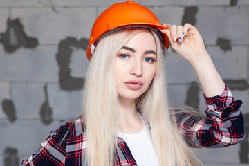 Beautiful sexy girl the designer foreman blonde in an orange construction helmet and jeans overalls. Concept of repair in house, female labor, photo session at the construction site