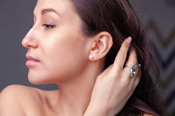 Closeup beautiful brunette girl with long hair in modern silver jewelry earrings, rings, bracelet, chain, necklace. Сoncept shooting store gentle, elegant, delicate, romantic bijouterie on model