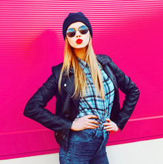 Wall Mural - Fashion portrait blonde cool girl sending sweet air kiss posing in rock black style jacket, hat posing on city street over colorful pink wall background