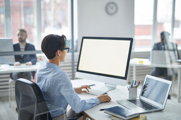 young brunette businesswoman looking at computer screen while sitting by desk and analyzing statisti