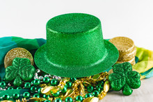 Green Sparkling Top Hat With Gold And Green Beads, Gold Coins, Green Shamrocks And Colorful Scarf In Background.  White Background.  Close Up View.
