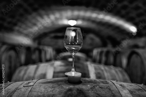 Fotografía Glass standing on barrel in wine cellar. Black & white photo.