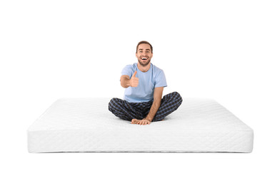 Wall Mural - Young man sitting on mattress against white background