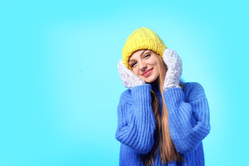 Poster - Portrait of emotional young woman in stylish hat, sweater and mittens on color background, space for text. Winter atmosphere