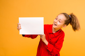 girl holding white sheet.Cute little girl with white sheet of paper.yellow background.copy spase.Little girl holding empty sheet of a paper