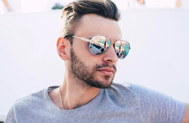 Deep water. Handsome boy with dark hair and smooth skin wearing grey t-shirt and sunglasses with a reflection of turquoise-colored sea water and a part of a holiday cruiser.