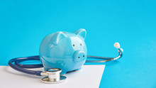 Piggy Bank With Stethoscope Isolated On Blue Background. Concept Of Financial Literacy. Creating And Maintaining A Budget. Keeping Their Finances On Track. Ruin Loan History