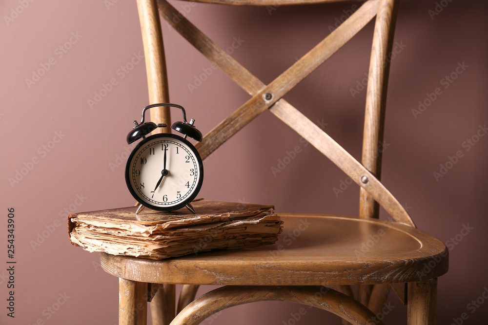 Alarm clock and old book on chair against color background