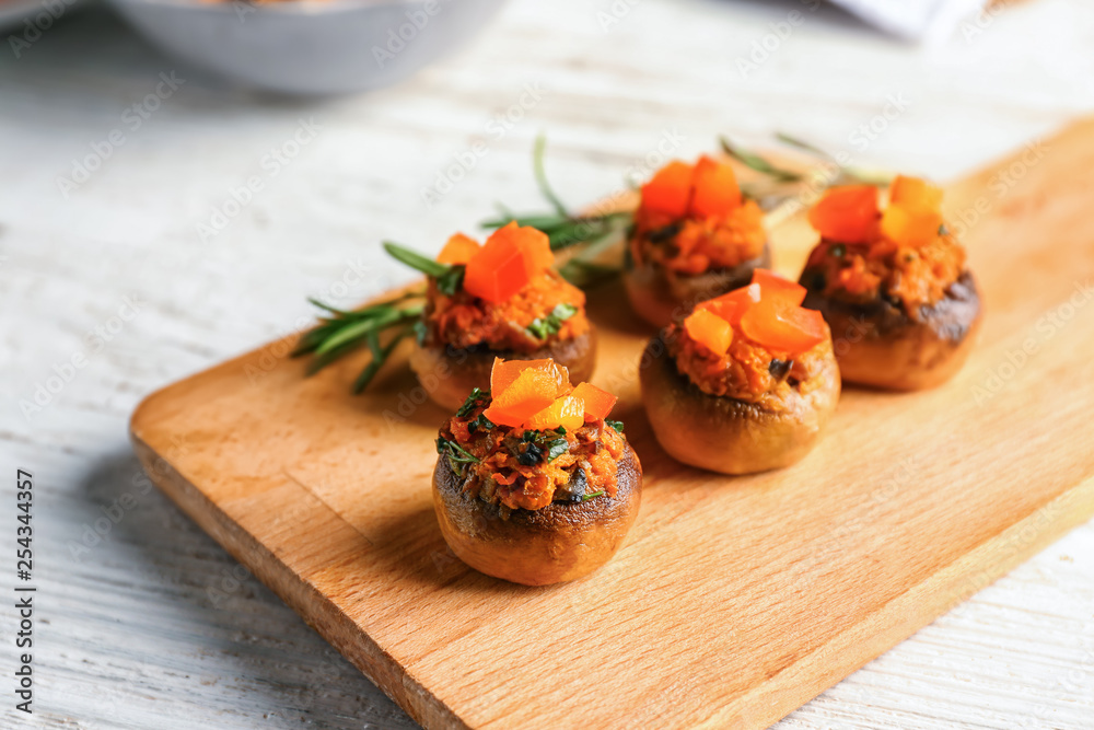 Wooden board with tasty stuffed mushrooms on white table