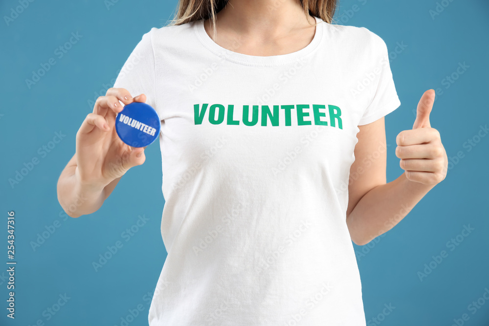 Young female volunteer with badge on color background