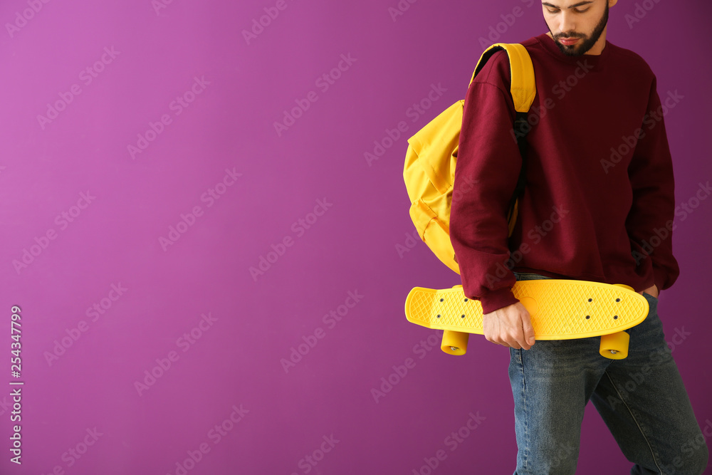 Fashionable young man with skateboard on color background