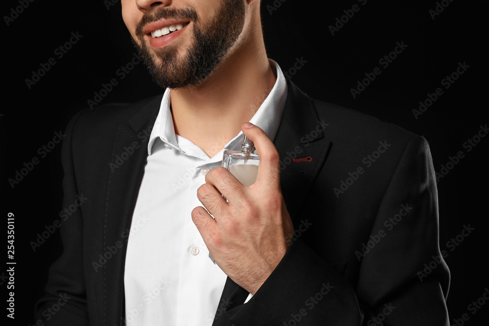 Handsome man with bottle of perfume on dark background, closeup