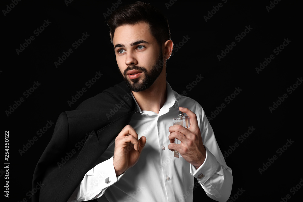 Handsome man with bottle of perfume on dark background