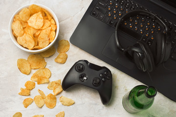 Wall Mural - Laptop, Gamepad, Headphones, Potato chips, Bottle of Beer on a light stone background. Concept of computer games and leisure