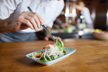 closeup of professional chef plating asian seafood dish in restaurant kitchen, copy space