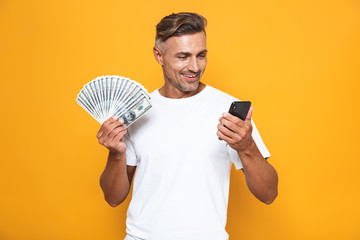 Wall Mural - Image of attractive guy 30s in white t-shirt holding cell phone and bunch of money