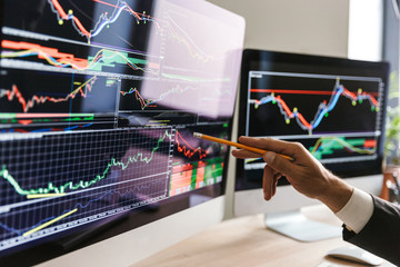 Fototapete - Hand of adult businessman sitting at table in office and pointing at graphics and charts on computer